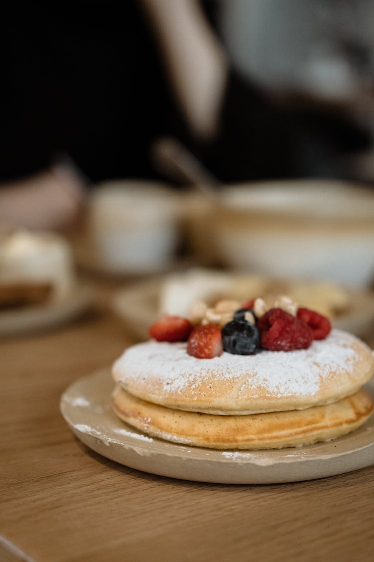 A Plate Of Pancake With Berry Toppings On A Wooden Surface