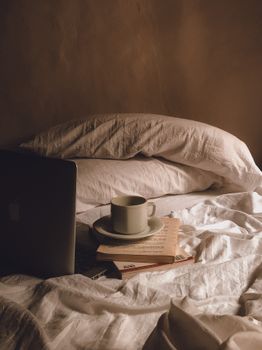 Relaxed bedroom setup with coffee, books, and a laptop on a bed, evoking comfort and leisure.