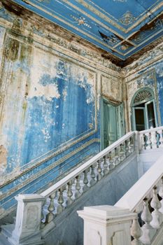 Stunning view of a neglected palace interior with peeling blue walls and grand staircase.
