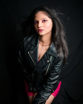 Elegant portrait of a woman in a black leather jacket with a dark studio background, showcasing fashion and style.