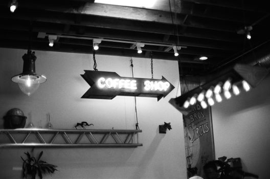 Black and white image of a neon coffee shop sign in a rustic interior with exposed beams.
