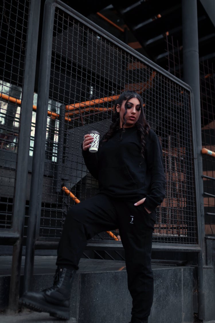 Woman In Black Sweatshirt And Pants Holding A Paper Cup