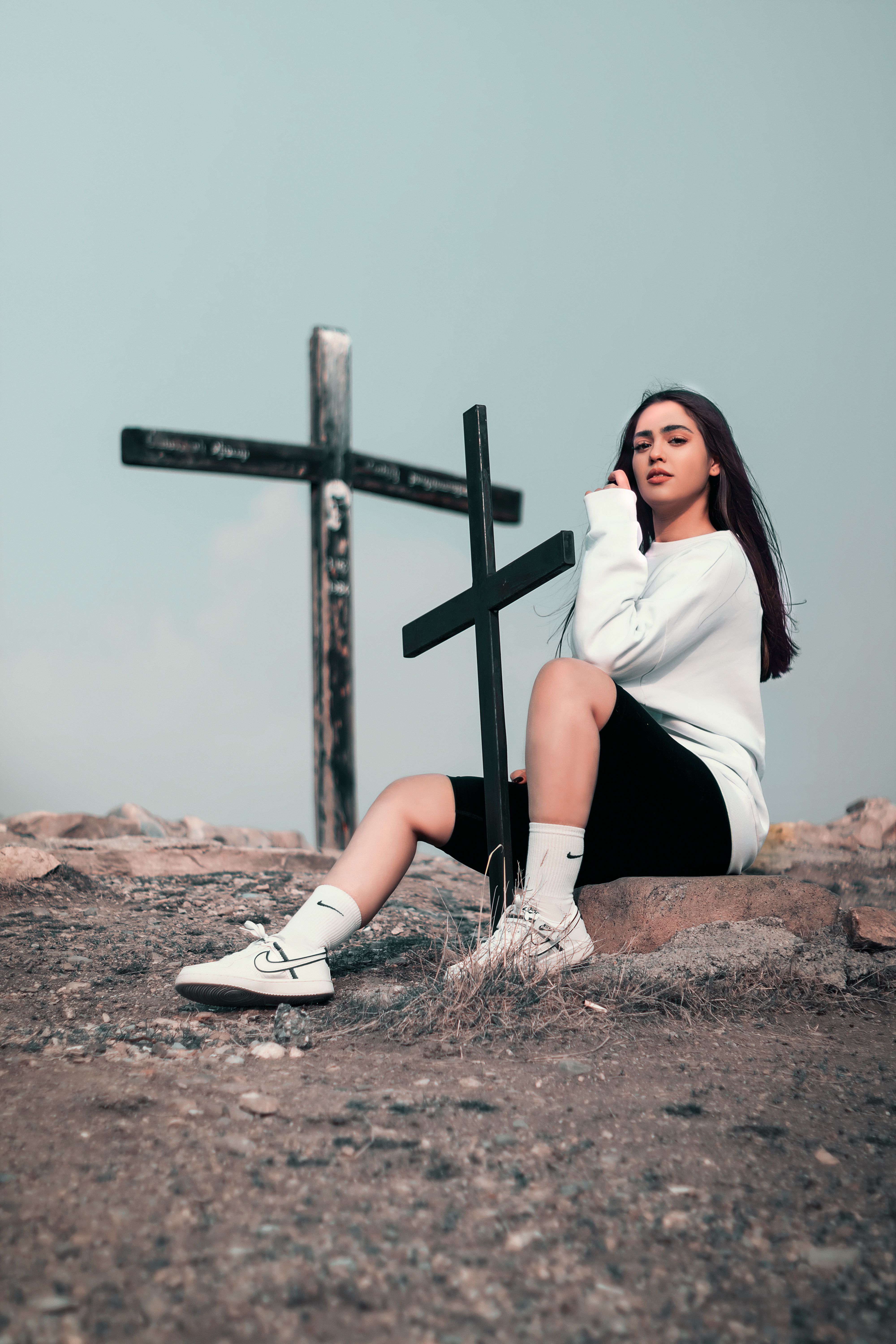 Young woman sitting near crosses in an outdoor setting, wearing casual attire.