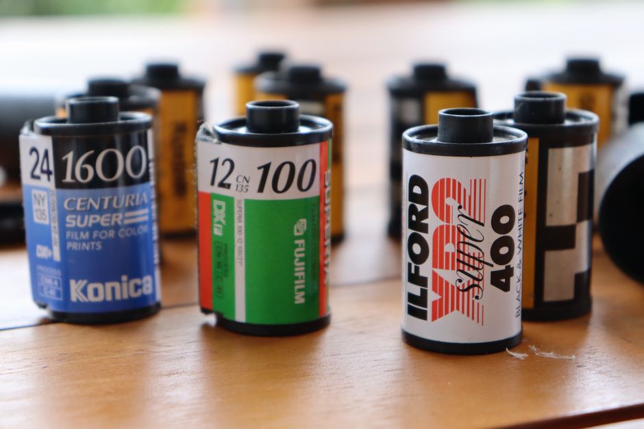 Três cartuchos de filme 35mm alinhados sobre superfície de madeira para comparação