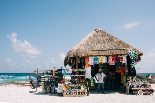 Free Beachfront market stall selling traditional clothing and souvenirs with ocean backdrop. Stock Photo