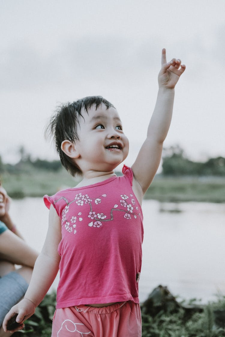 Baby Girl Wearing Pink Tank Top Pointing Finger To The Sky