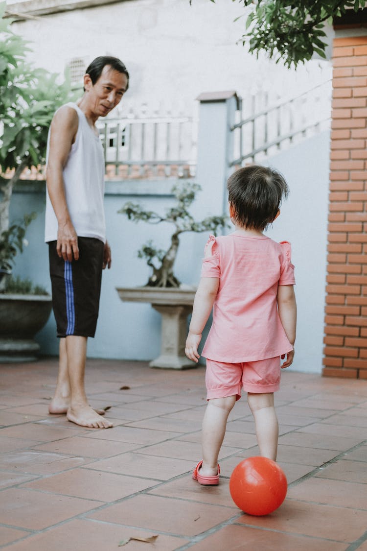 Man And Child Playing With Ball In Yard