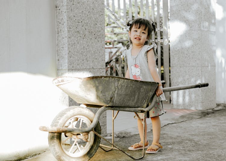 Little Girl Standing By A Wheelbarrow