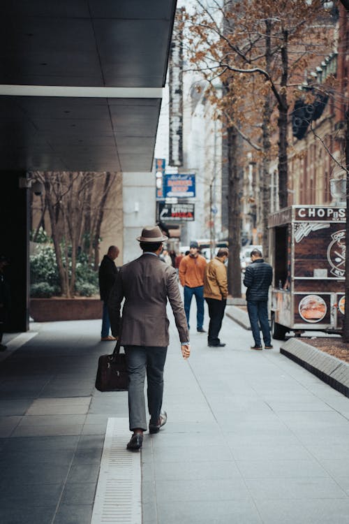 Back View of Man with Hat Walking on City Street