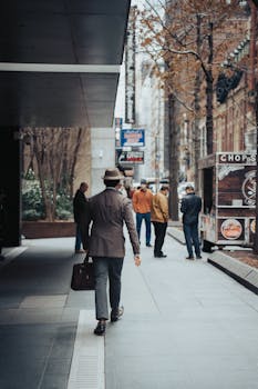 Man in a hat walking along a city street with a suitcase, city life captured.