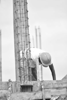 Grayscale image of a construction worker bending over a steel frame, taken outdoors.