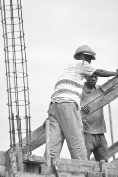Black and white image of two construction workers wearing safety gear and helmets at a building site.