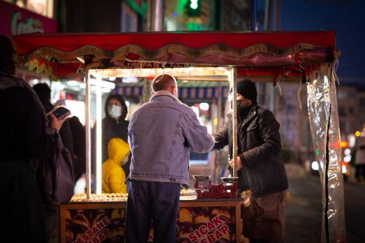 A bustling street food stall in Istanbul's lively night market with diverse people enjoying snacks.