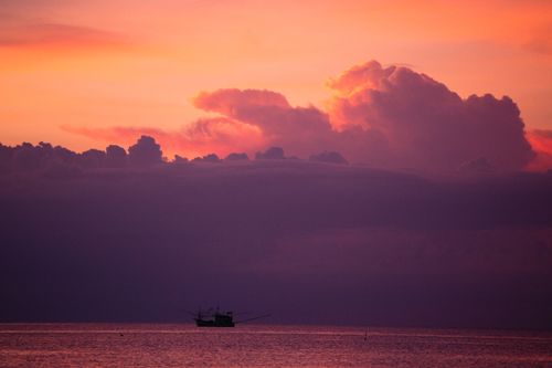 Free Silhouetted boat during a vibrant sunset over the sea with dramatic clouds. Stock Photo