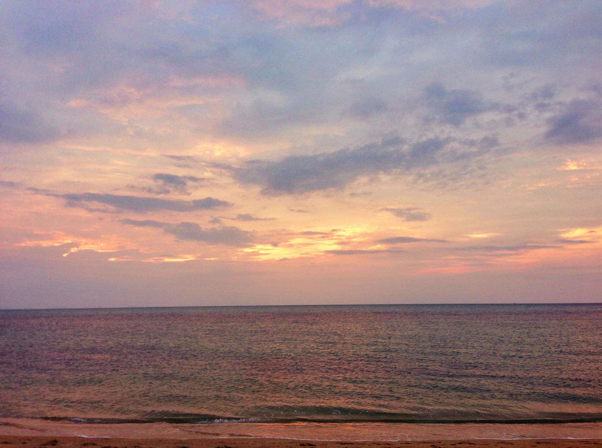 Tranquil ocean view at sunrise with soft pastel sky hues and peaceful waves.