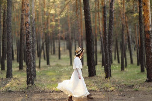 Free A Woman in White Dress Walking Near the Trees Stock Photo