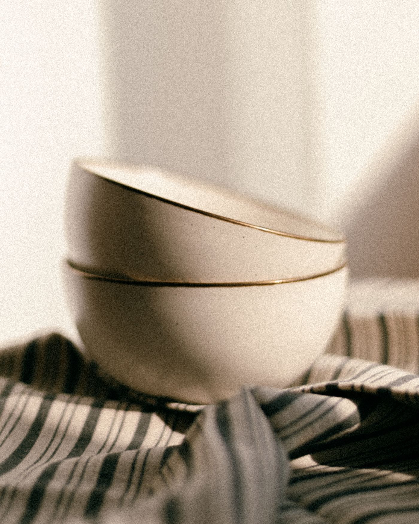 Stacked ceramic bowls arranged on draped fabric with soft natural light and visible handmade texture