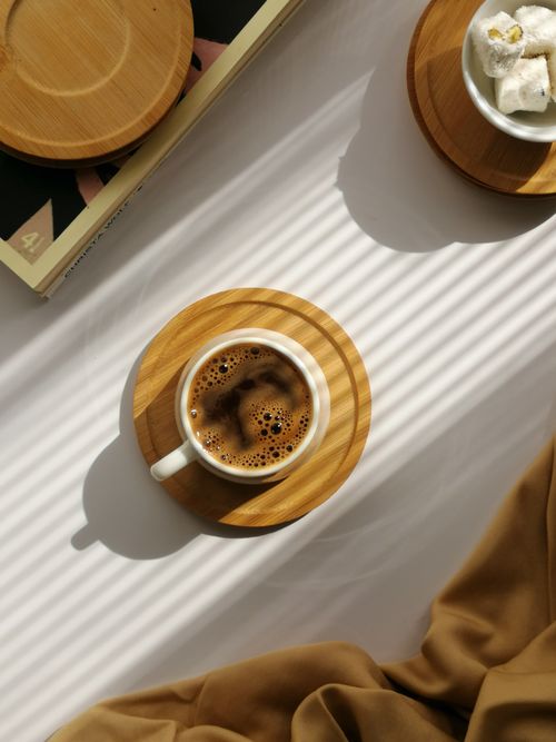 Free Overhead view of a cup of coffee on a wooden coaster with sunlight casting shadows. Stock Photo