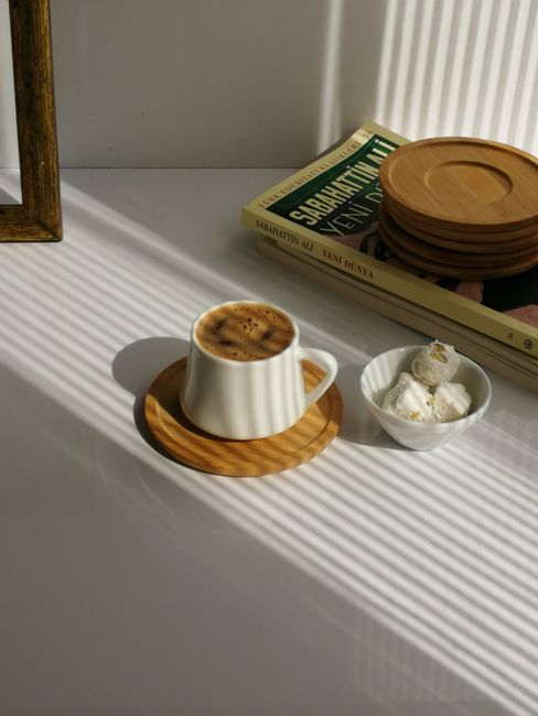 Inviting morning setup with a cup of coffee, book, and dessert in sunlight.