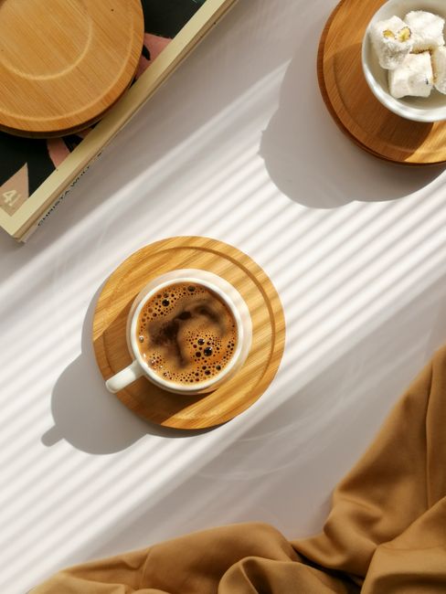 Warm coffee cup on wooden coaster in bright sunlight casting shadows.