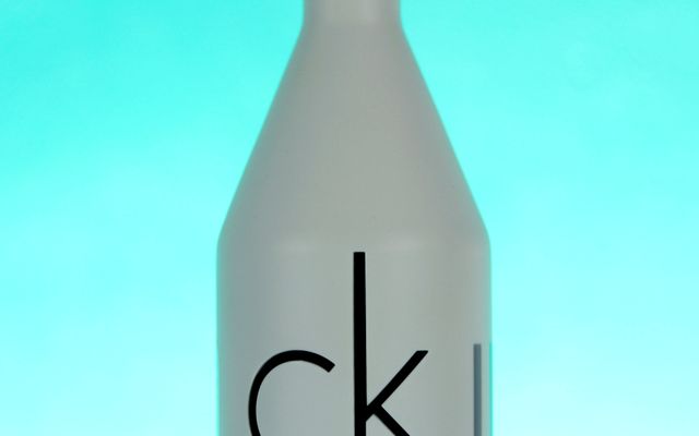 Frosted white cologne bottle with a large black ck logo against a bright turquoise background