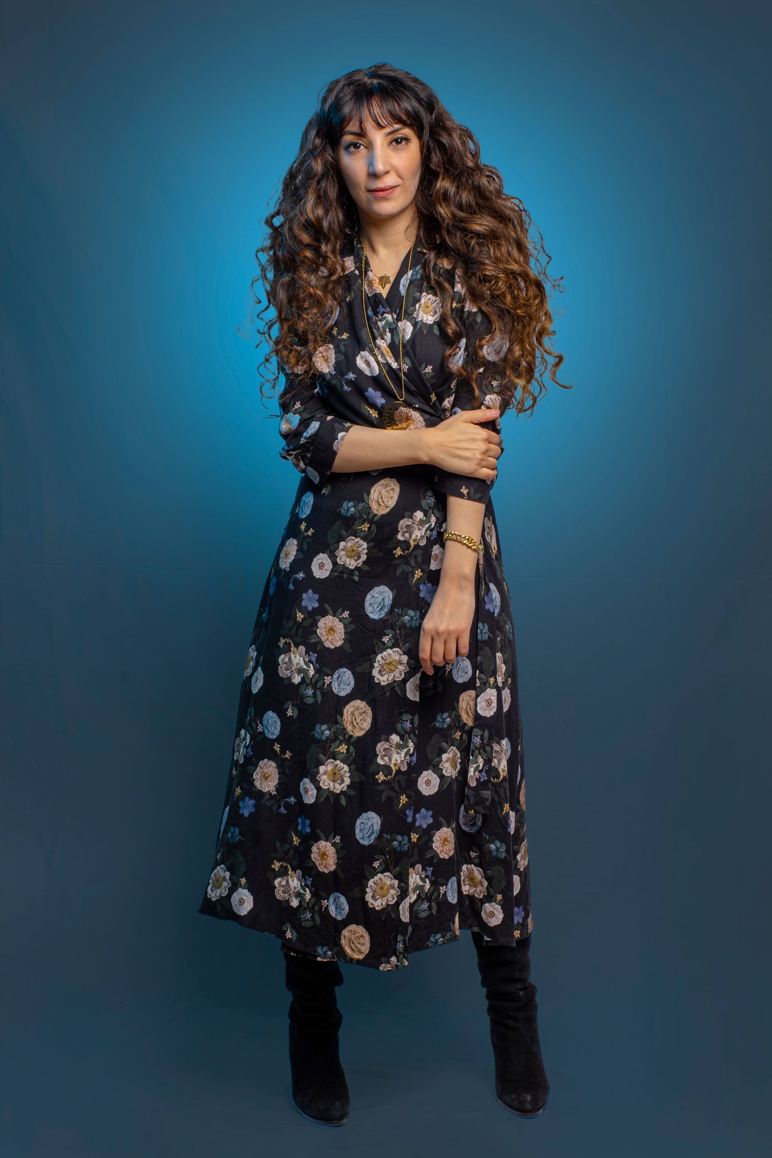 Elegant woman with wavy hair in a floral dress posing against a blue background in a studio.