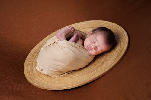 Free Adorable newborn baby peacefully sleeping in a woven basket on brown background. Stock Photo