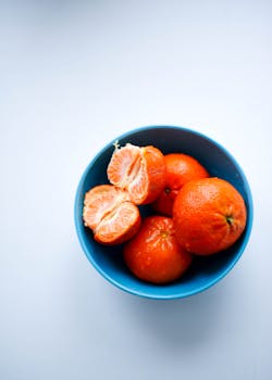 Fresh tangerines in a blue bowl captured in a vibrant studio shot from above.