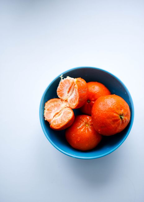 Fresh tangerines in a blue bowl captured in a vibrant studio shot from above.