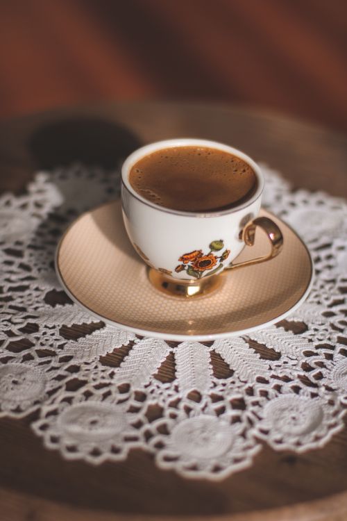 Free A delicate ceramic cup of coffee placed on a beautiful lace doily, captured with warm lighting. Stock Photo