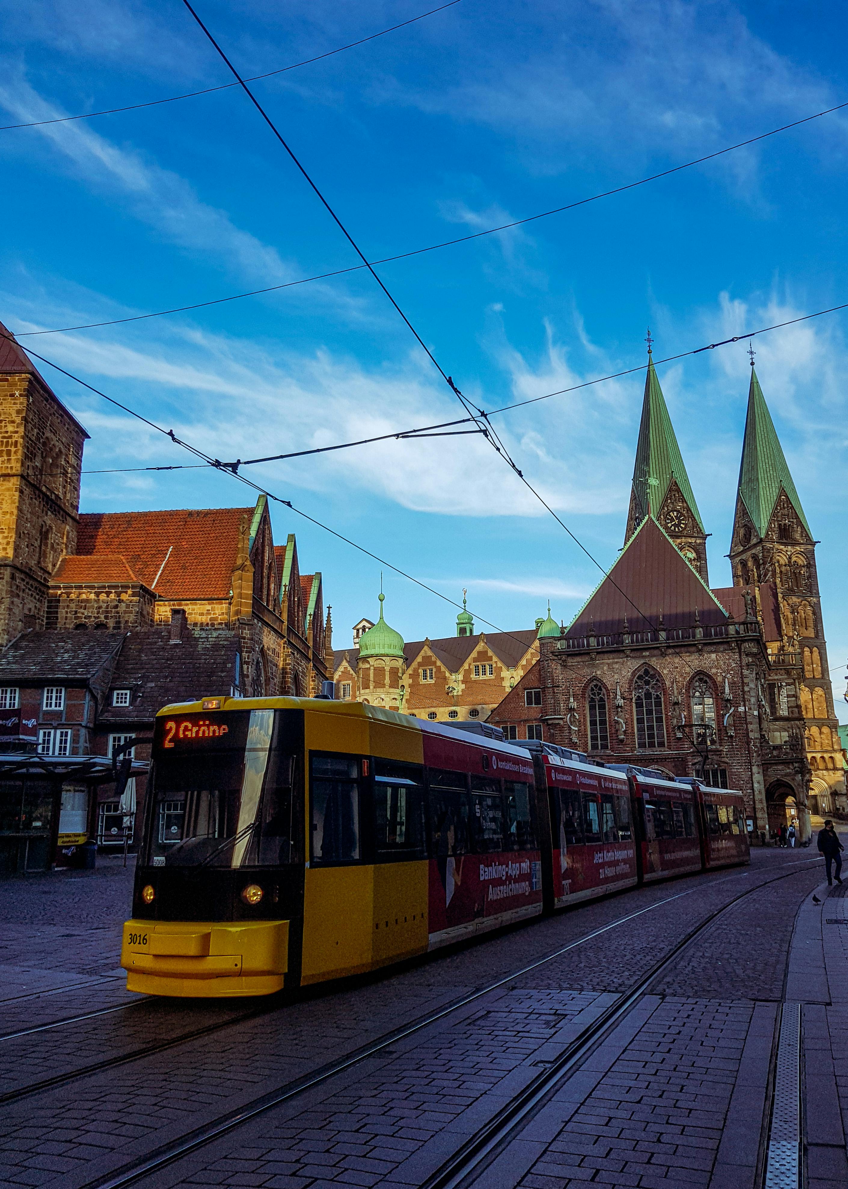 Free A vibrant yellow tram traverses the historic streets of Bremen, Germany, near St. Peter's Cathedral. Stock Photo