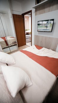 A serene modern bedroom with warm decor and a television displaying a sports game.