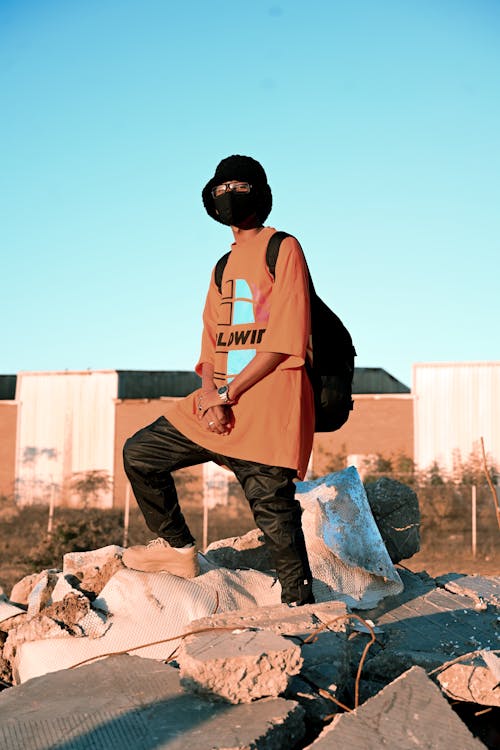 A Person in Orange Shirt and Black Pants Wearing Facemask Standing on White Rock