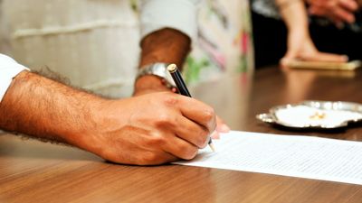Persona con reloj en la muñeca firma a mano un documento sobre una mesa de madera, sobre testamento en Chile