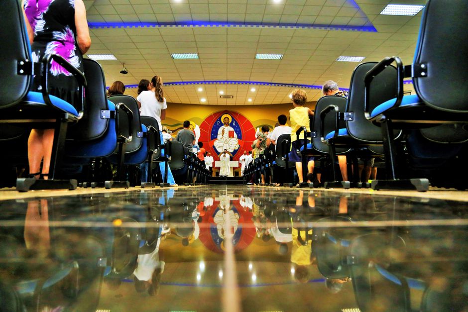 A church service with people seated, colorful reflection on polished floor, vibrant interior.