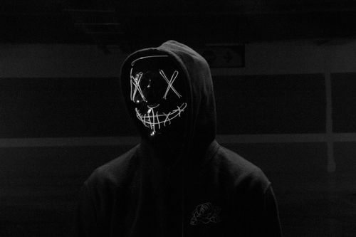 Free Eerie image of a person in a glowing LED mask and hoodie in a dark setting. Stock Photo