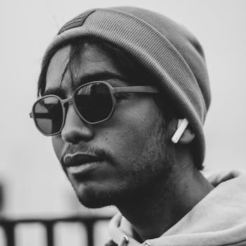 Stylish black and white portrait of a man wearing a beanie, sunglasses, and earphones.