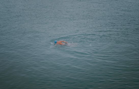 A male swimmer in a blue cap swims in open water, competing in a race.