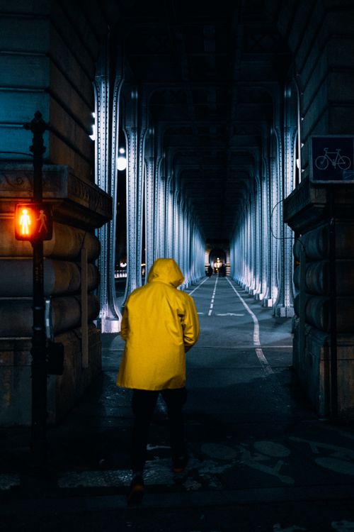 Free Person in yellow coat walking under a bridge at night, creating a dramatic urban scene. Stock Photo