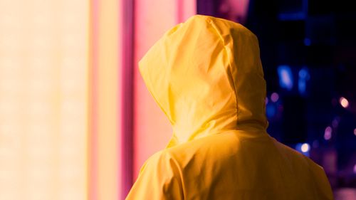 Free Back view of a person in a yellow raincoat, facing bright colorful lights. Stock Photo