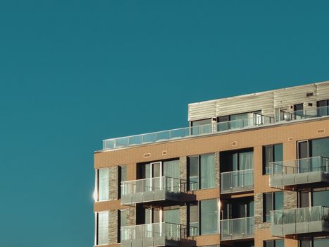 Stylish urban apartment building exterior with glass balconies under a clear sky.