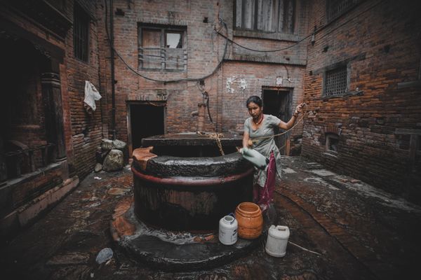 A woman drawing water from a traditional stone well in a Nepali village