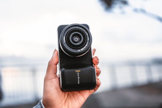 A close-up image of a hand holding a digital camera outdoors, showcasing its lens and control.