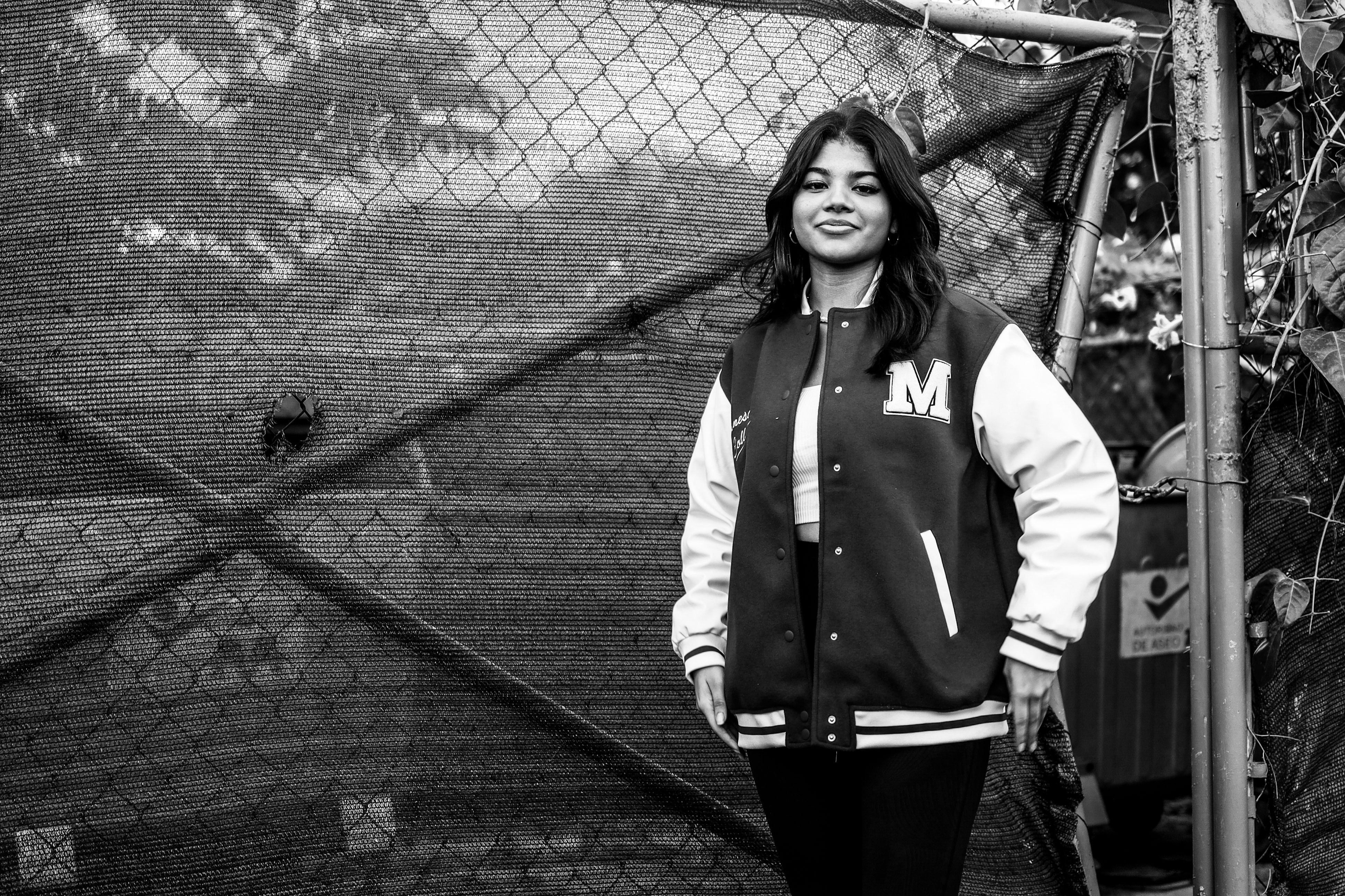 Stylish young woman in varsity jacket, standing confidently outdoors.