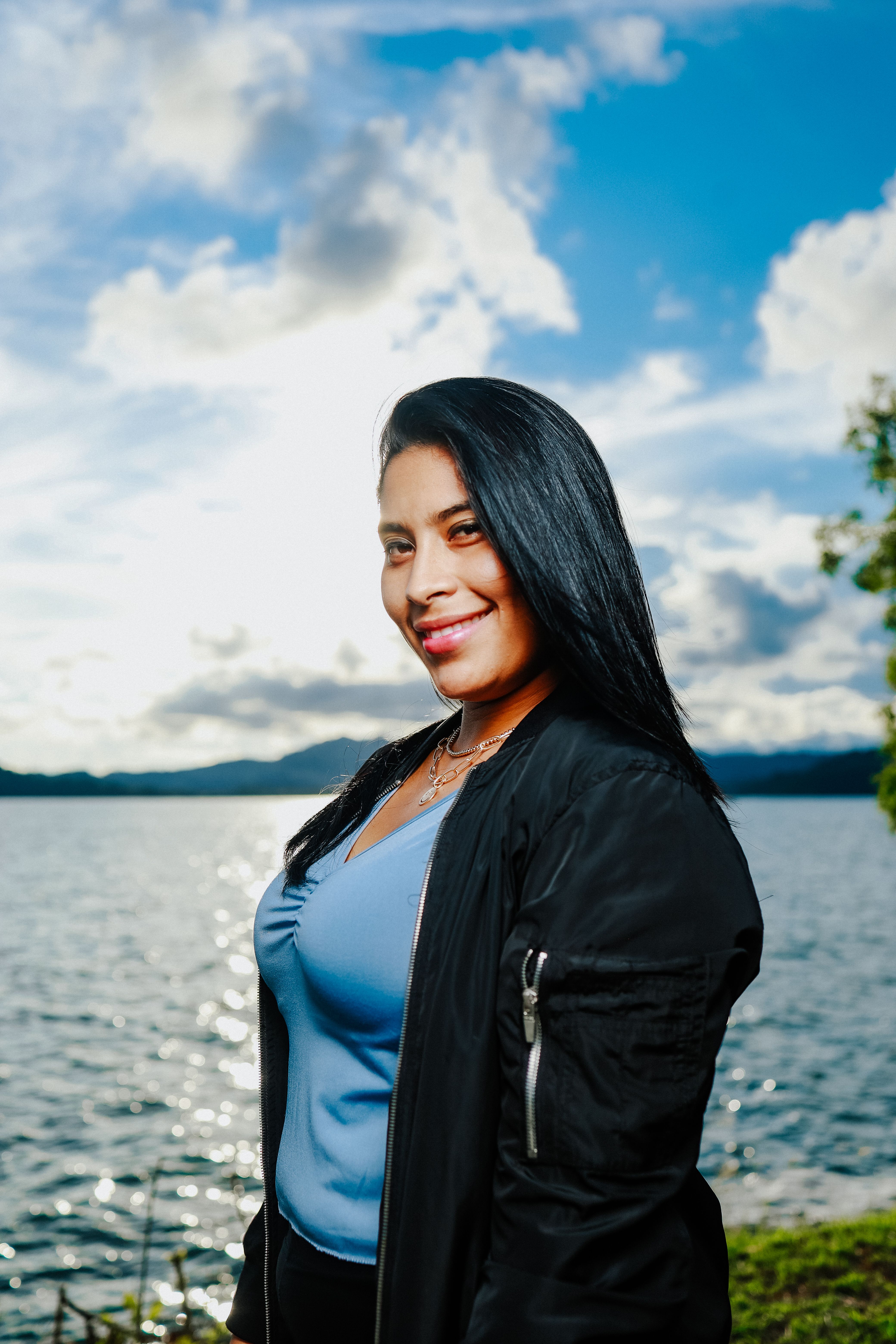 Happy woman with long hair smiling by a scenic lake during sunset.
