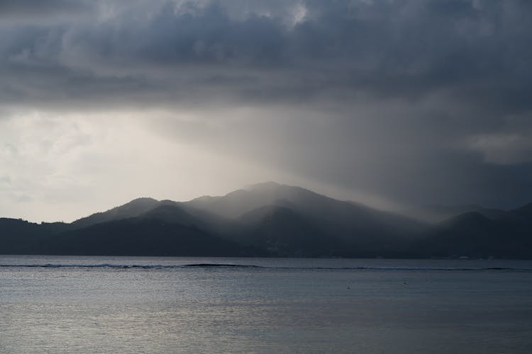 A Body Of Water Near Mountain Under Cloudy Sky