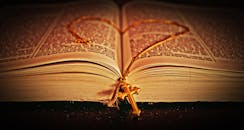 一本打开的圣经特写，书页上放着一条金色十字项链，营造出宁静而富有反思的氛围