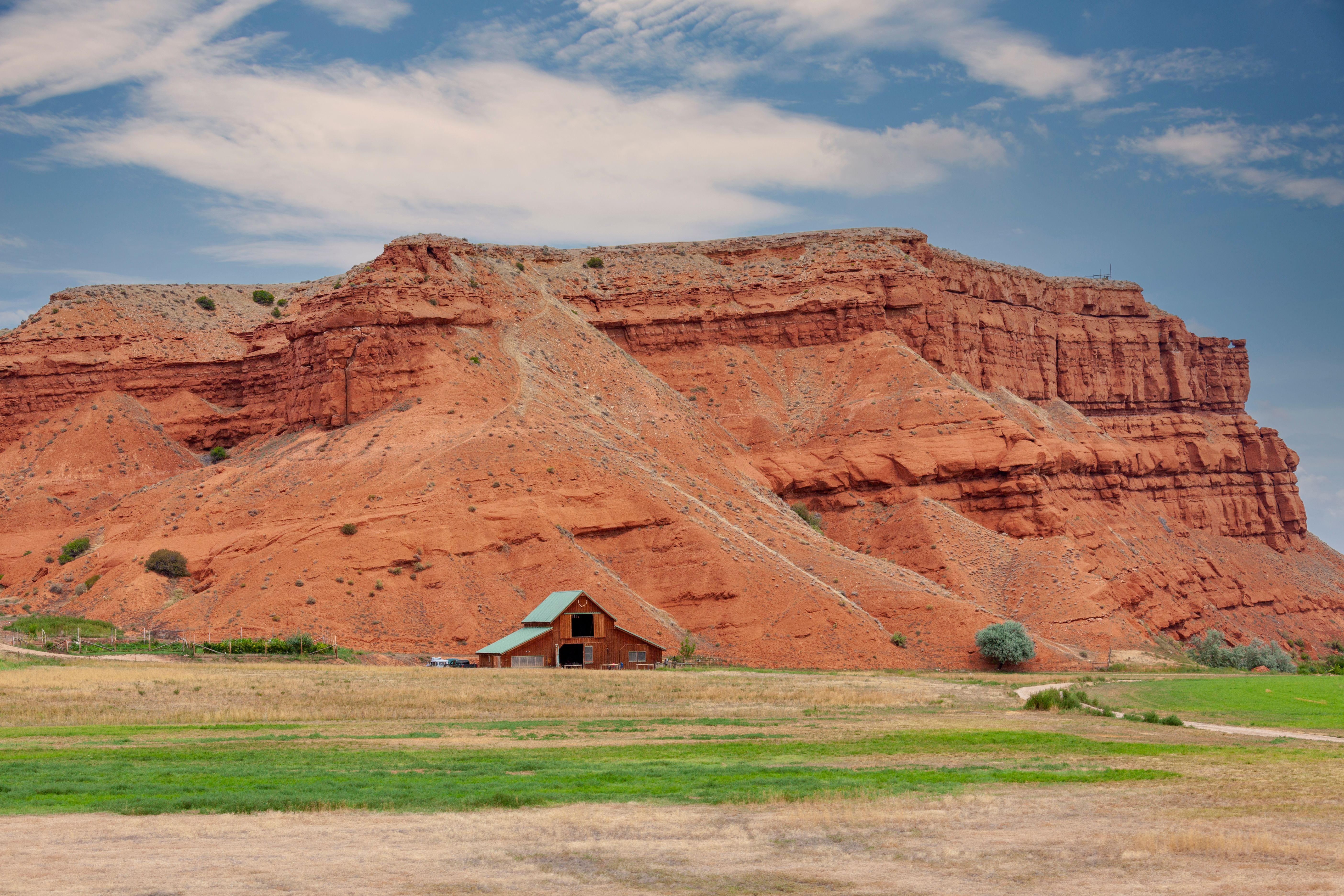 A scenic view of red cliffs with a wooden barn nestled below in Wyoming, USA.
