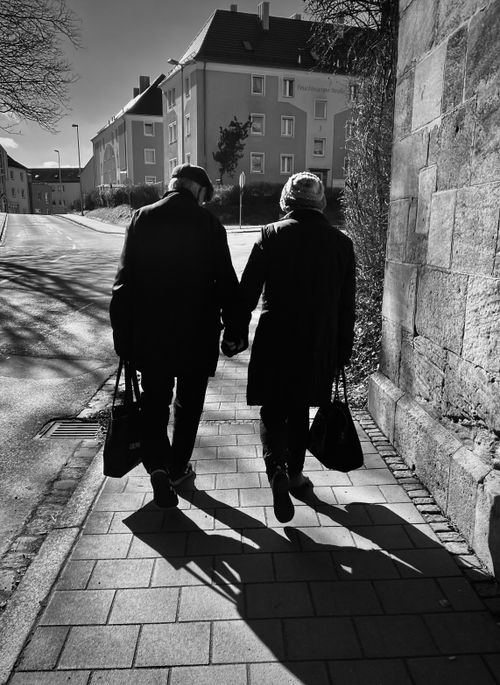 Free Black and white photo of an elderly couple walking hand in hand in Ansbach, Germany, creating a romantic street scene. Stock Photo