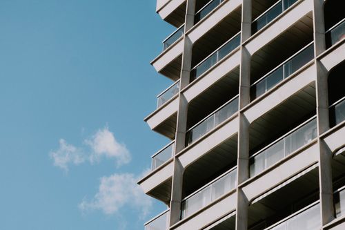 Free Perspective view of a modern high-rise building featuring balconies against a clear blue sky. Stock Photo